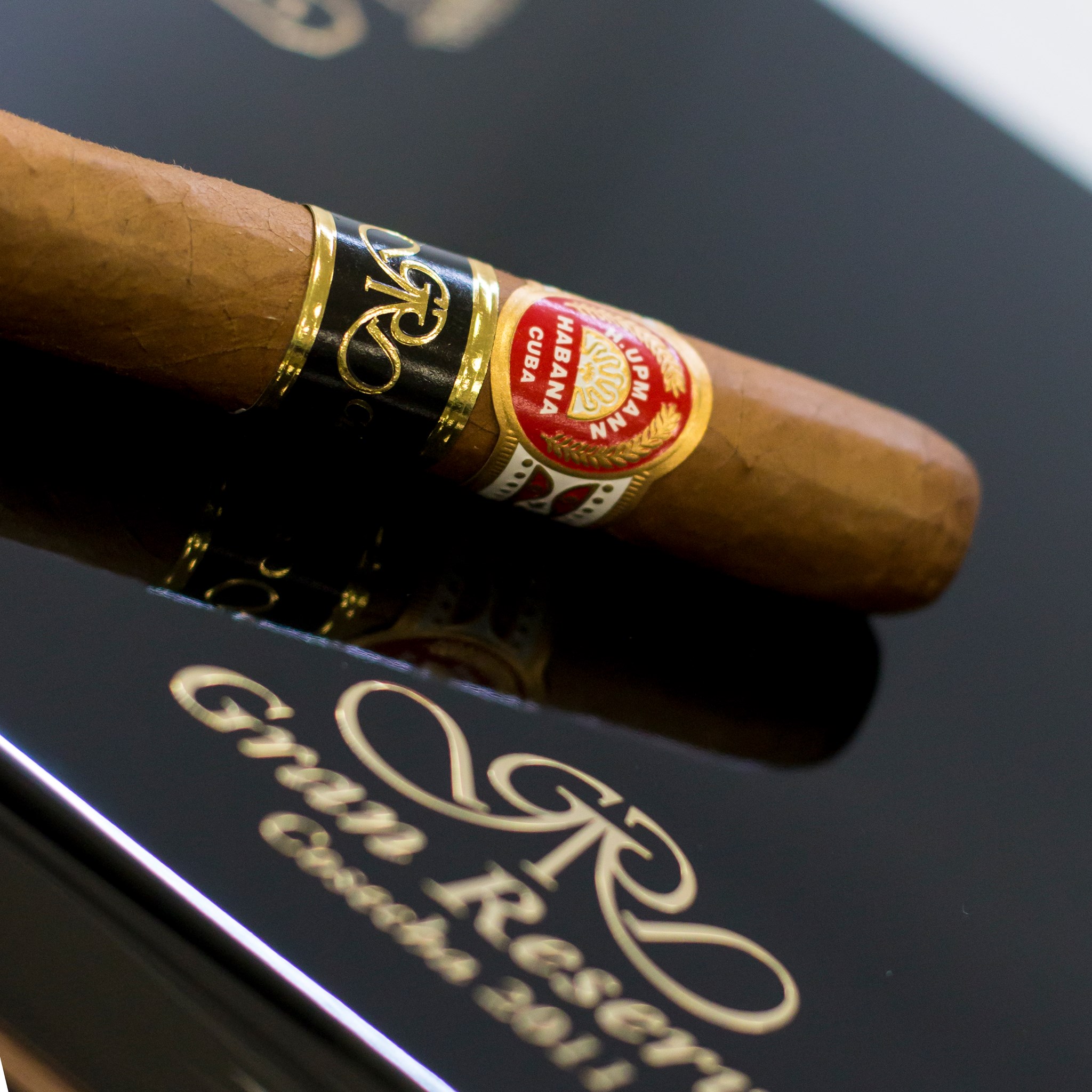 A Cohiba 50 Aniversario at rest on a polished mahogany desk, leather books and a brass lamp behind